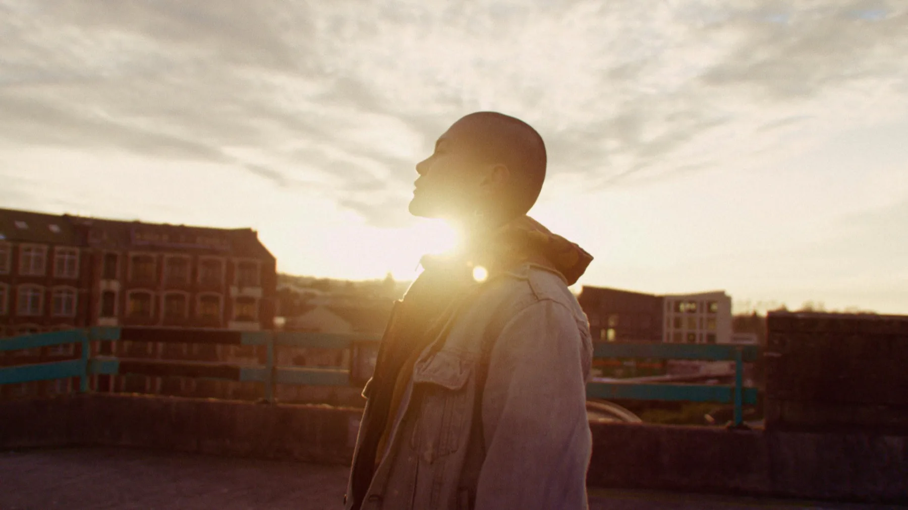 A child standing in warm sunlight on a rooftop, looking toward the horizon
